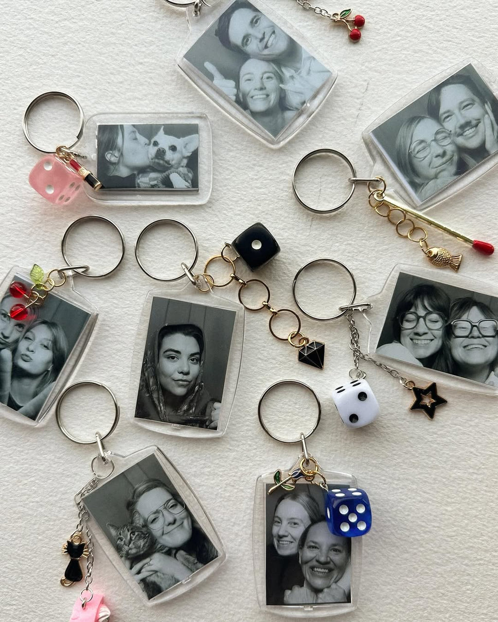 Collection of keychains with black and white photos and various charms on a textured surface.