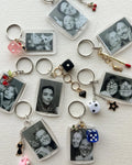 Collection of keychains with black and white photos and various charms on a textured surface.