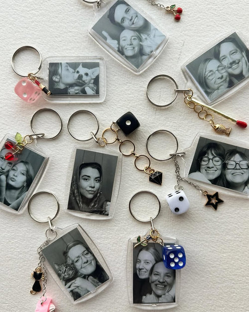 Collection of keychains with black and white photos and various charms on a textured surface.