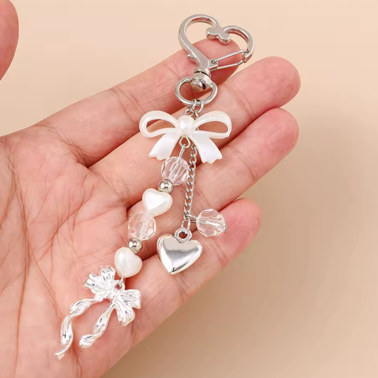 Silver keychain with decorative elements held in a hand against a beige background