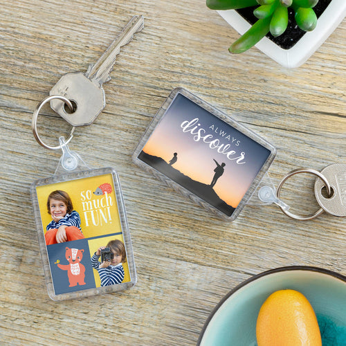 Two keychains on a wooden surface with one featuring a photo of children and the other with a motivational quote.