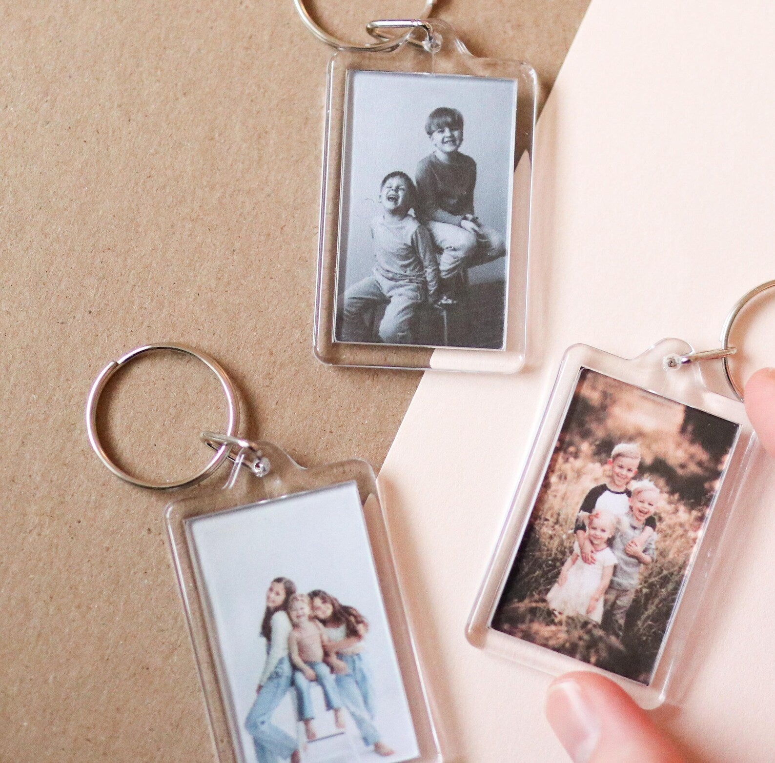 Three keychains with printed photos of people on a beige background
